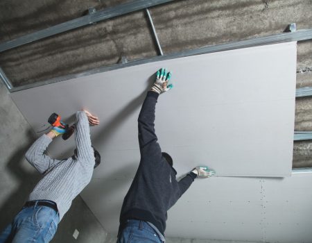 Workers fitting panel into frame of ceiling.