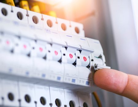 Male hand switching on the electric switch box with automatic fuses. Electrician installing electric cable wires and fuse switch boxes. Multimeter in hands of electricians.